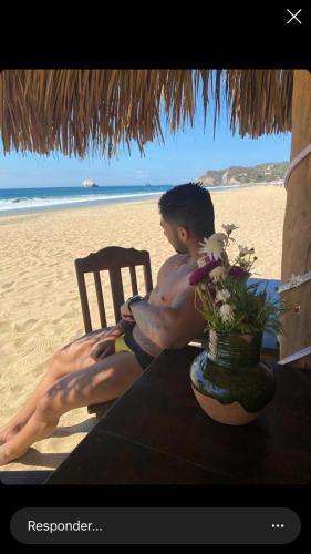a boy sitting in a chair on the beach at La Máxima & LGBT in Zipolite