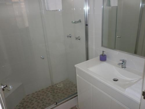 a white bathroom with a shower and a sink at Oceana Holiday Units in Coffs Harbour
