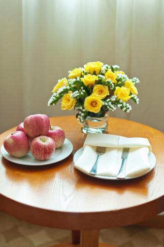 a table with apples and a vase of flowers and a plate at Muong Thanh Holiday Da Lat Hotel in Da Lat