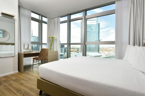 sypialnia z białym łóżkiem, biurkiem i oknami w obiekcie Torre Galfa Milano Luxury Apartments | UNA Esperienze w Mediolanie
