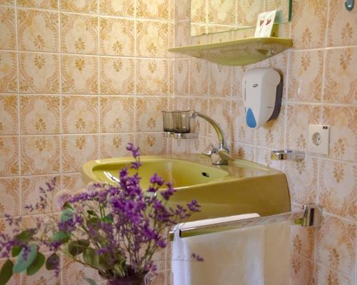 a bathroom with a sink and a vase of purple flowers at Mitten in der Welt - GH Roither in Herzogsdorf