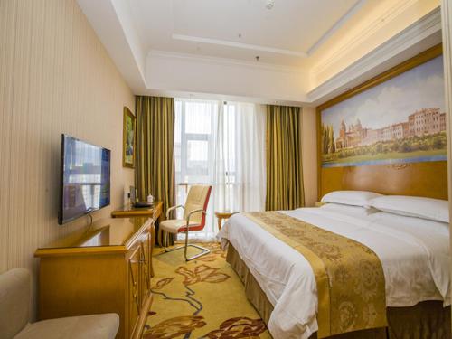 una camera d'albergo con un grande letto e una scrivania di Vienna Hotel Guizhou Bijie Chuangmei Century City a Bijie