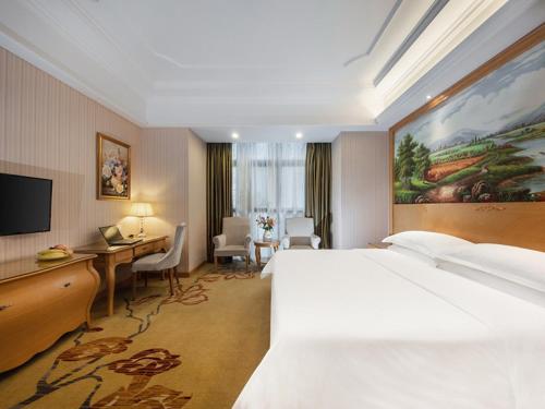 ein Hotelzimmer mit einem großen Bett und einem Schreibtisch in der Unterkunft Vienna International Hotel Fuzhou Cangshan Wanda in Fuzhou