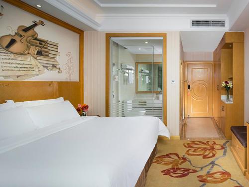 a bedroom with a large bed and a guitar on the wall at Vienna Classic Hotel Ganzhou Meilin in Ganzhou