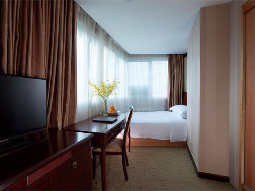 ein Hotelzimmer mit einem Bett, einem Schreibtisch und einem TV in der Unterkunft Vienna Hotel Shenzhen Fenghuang Road in Shenzhen