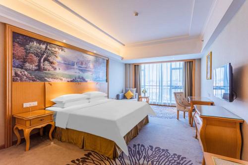 佛山市にあるVienna Hotel Foshan Airportの大きなベッドとデスクが備わるホテルルームです。
