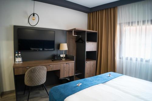 ein Hotelzimmer mit einem Bett und einem Schreibtisch mit einem TV in der Unterkunft Hotel Palatinus in Sopron