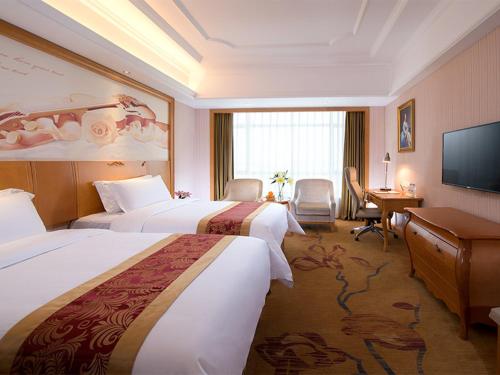 a hotel room with two beds and a desk and a television at Vienna International Hotel Huazhou East Beijing Road in Dongshan