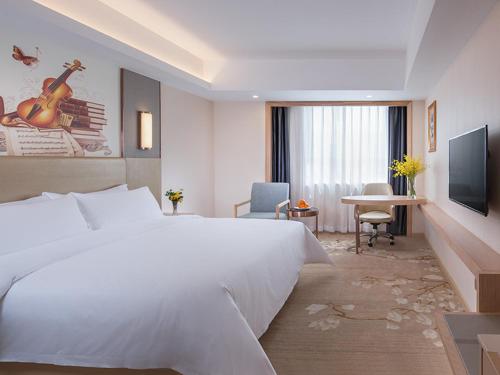 a hotel room with a large white bed and a television at Vienna Hotel Shenzhen Pingji Ave in Longgang