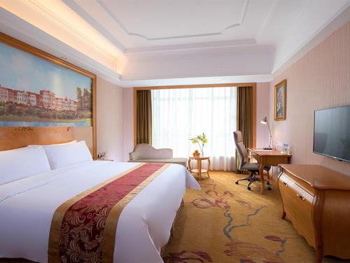 a hotel room with a large bed and a desk at Vienna International Hotel Huazhou East Beijing Road in Dongshan