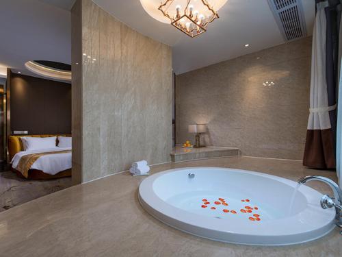 a bathroom with a tub with a bed in the background at Vienna International Hotel Diecai Wanda High Speed ​​Rail Station in Guilin