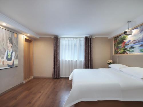 a bedroom with a large white bed and a painting at Vienna International Hotel Jingdezheng People Square in Jingdezhen