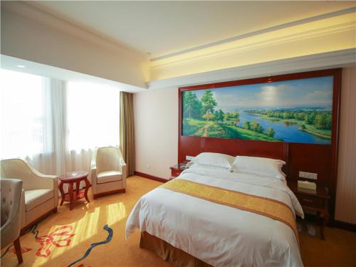 een hotelkamer met een groot bed en een groot schilderij aan de muur bij Vienna International Hotel Shandong Weihai Rongcheng in Rongcheng