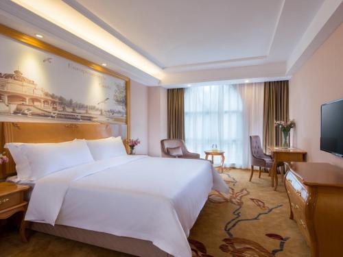ein Hotelzimmer mit einem großen weißen Bett und einem TV in der Unterkunft Vienna Hotel Shenzhen Luofang in Shenzhen