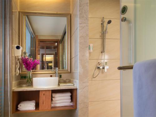a bathroom with a sink and a mirror and a shower at Vienna International Hotel Shenzhen Longgang Lilang in Longgang