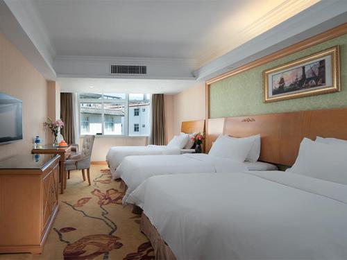 a hotel room with three beds and a television at Vienna International Hotel Lijiang Yuxue Avenue in Lijiang