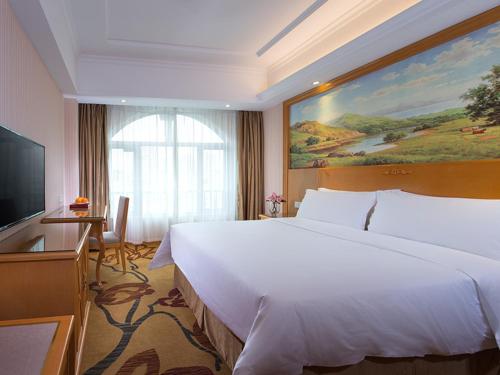 una camera d'albergo con un grande letto bianco e una TV di Vienna Hotel Shenzhen Dalang Clothing Base a Bao'an