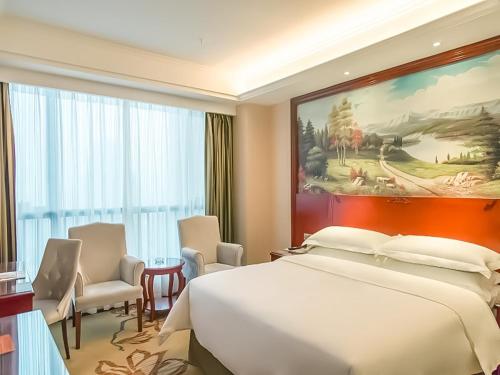 a bedroom with a white bed and a large painting at Vienna Hotel Jian People Square in Ji'an