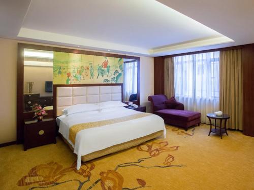 a bedroom with a large bed and a purple chair at Vienna Hotel Lufeng Peopole Road in Lufeng