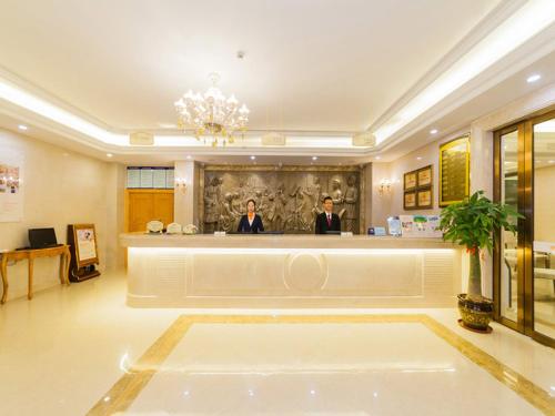 two people standing at a counter in a hotel lobby at Vienna 3 Best Hotel Fuzhou Fuma Road Ziyang in Fuzhou