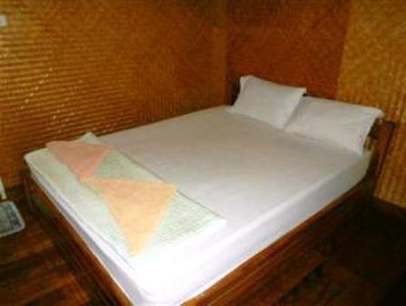 a small bed with white sheets and pillows at Tamarind Guesthouse in Kanchanaburi