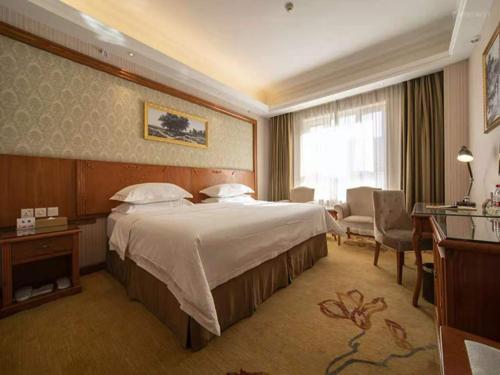 a hotel room with a large bed and a desk at Vienna Hotel Xinjiang Yining Shanghai City in Yining