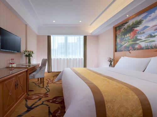 ShengzhouにあるVienna Hotel (Shengzhou Bada Hotel)の大きなベッドとデスクが備わるホテルルームです。