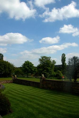a grassy yard with a stone wall and trees at Best Western Sysonby Knoll Hotel in Melton Mowbray
