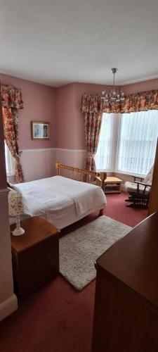 a bedroom with a bed and a table and two windows at Beach Cottage in Shanklin