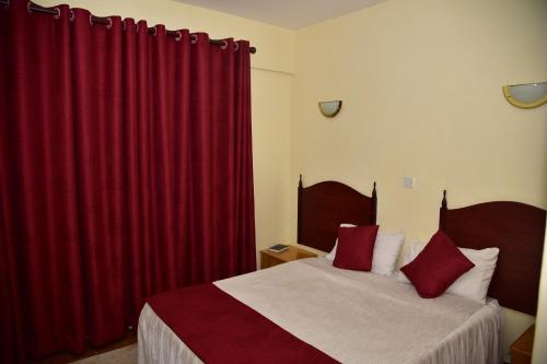 a bedroom with two beds with red curtains at Klique Hotel Eldoret in Eldoret
