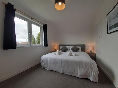 a white bedroom with a large bed and a window at Carvetii - Jade House - 3 bed House sleeps up to 8 in Kelty
