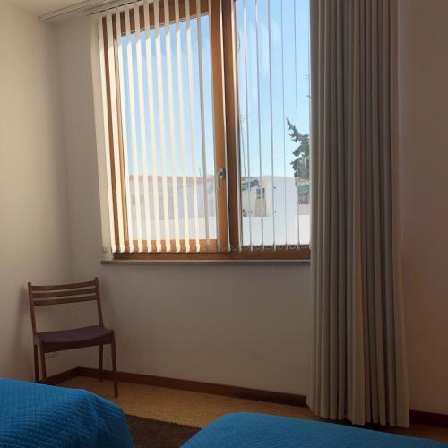 a bedroom with a bed and a window with a chair at Sossego Salgado in Tavira