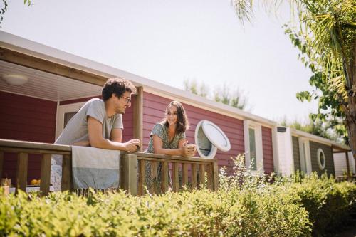 a man and a woman sitting on a fence in front of a house at Camping Sènia Caballo de Mar in Pineda de Mar