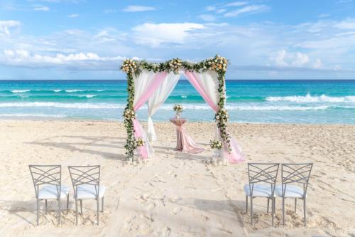 a wedding arch on the beach with two chairs and a table at Hotel NYX Cancun in Cancún