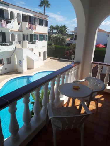 een balkon met een zwembad en een tafel en stoelen bij Apartamentos Xoroi in Cala'n Porter