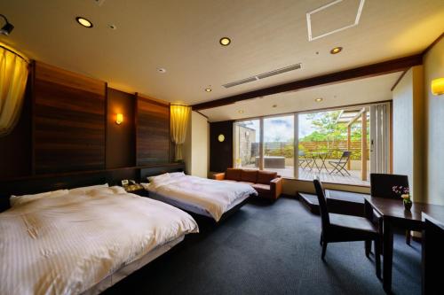 a bedroom with two beds and a desk and a window at Hotel Beppu Pastoral in Beppu