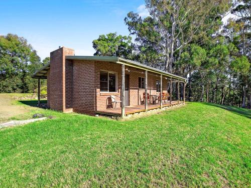 a brick house with a wrap around porch on a grass field at Braeside Cabin One Pinkwood in Central Tilba
