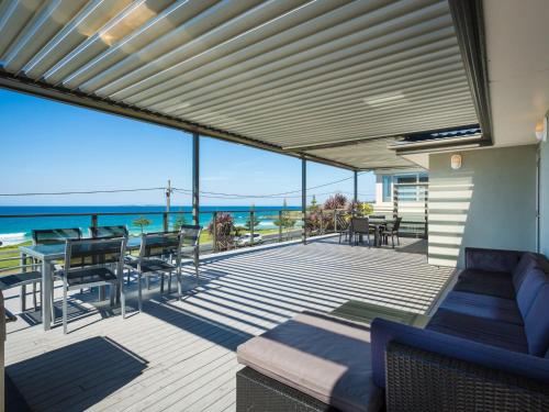 
a patio area with chairs, tables, and a balcony at 81 Dalmeny Drive - Beach House in Kianga
