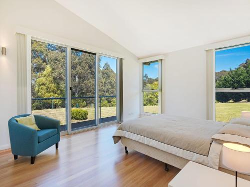 a bedroom with a bed and a chair and windows at Bayview Ringlands in Narooma
