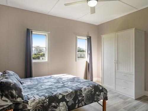 ein Schlafzimmer mit einem Bett und zwei Fenstern in der Unterkunft The Inlet Cottage in Narooma