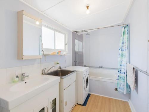 a white kitchen with a sink and a washing machine at Pet Friendly Beach Cottage @ Ballingalla in Narooma