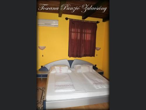 a bed in a room with a yellow wall at Toscana Panzió in Zalacsány