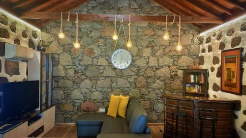 a living room with a couch and a clock on a stone wall at Casa Leon in Tejeda