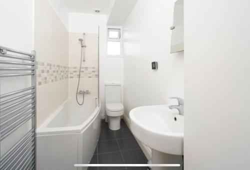 a white bathroom with a sink and a tub and a toilet at 35 mins to central London. 3 bedrooms. 2 bathrooms with garden in London