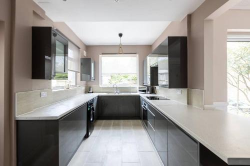 a large kitchen with black cabinets and a sink at The Cumbria House 5 bedroom House Stay in London