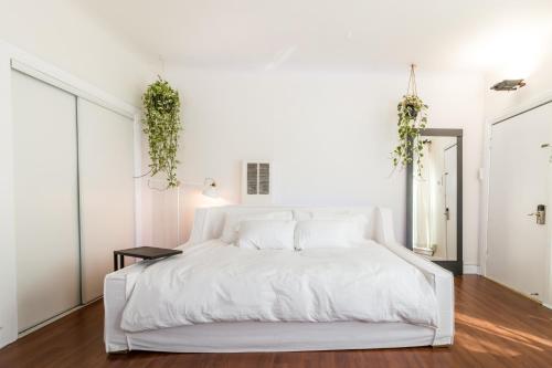 a white bedroom with a white bed with plants on the wall at Sunny Boho Chic West Hollywood Flat! in Los Angeles