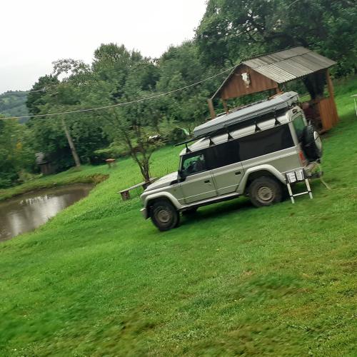 a green jeep parked in a field next to a river at RUSTIC SEJOUR,Roşia Montana in Roşia Montană