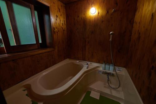 a bathroom with a tub with a shower and a window at SUNNSNOW Loghouse in Otari