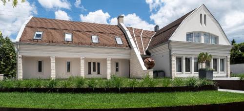 a white house with a brown roof and green grass at Hotel Bestseller in Kecskemét