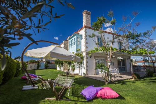 a house with a lawn with chairs and an umbrella at Deniz Kabugu Hotel in Alacati